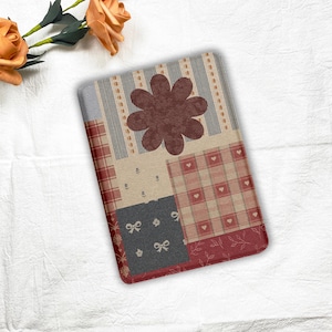 Könnte beinhalten: Eine rechteckige dekorative Matte im Patchwork-Stil mit einer großen, dunkelroten Blume in der Mitte. Die Matte weist verschiedene Muster auf, darunter Streifen, Karos, Schleifen und Herzen, in Rot-, Beige- und Grautönen. Die Ränder der Matte sind dunkler Rot.