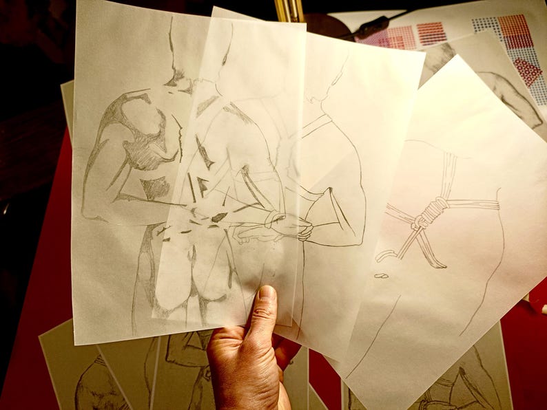 Pu&ograve; includere: Una mano tiene in mano diversi fogli di carta traslucida con schizzi a matita della forma umana. I disegni raffigurano figure in varie pose, con un focus sui dettagli anatomici e le proporzioni del corpo. Gli schizzi sono in bianco e nero.