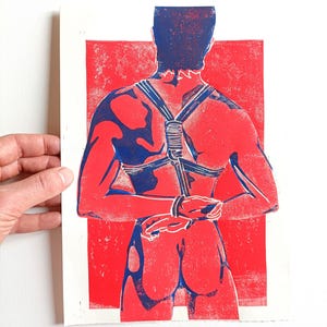 Pu&ograve; includere: Una stampa rossa e blu raffigurante una persona vista da dietro, legata con corde e cinghie. La figura &egrave; posta su uno sfondo rosso, con la corda e le cinghie in blu. La stampa &egrave; su carta bianca.