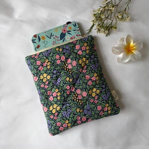 May include: A quilted fabric pouch featuring a dark navy blue background with a dense pattern of pink, yellow, and purple flowers and green leaves. A light blue floral notebook is partially inserted into the zippered opening of the pouch.