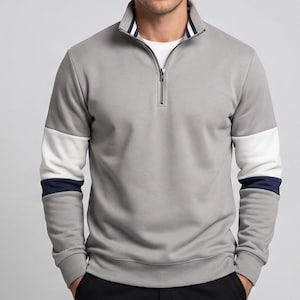 Peut inclure: Un sweat-shirt gris à fermeture éclair quart de zip avec des accents blancs et bleu marine sur les manches. Le col présente des rayures bleu marine et blanches. Le modèle porte un sous-vêtement blanc.