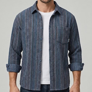 以下が含まれることがあります： 青いストライプのボタンダウンシャツ。胸ポケットとロールアップされた袖が付いています。白いクルーネックTシャツの上に着用されています。シャツは青とグレーの色合いの縦縞模様です。