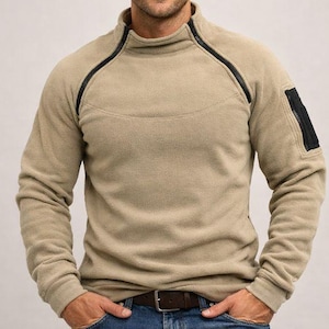 Peut inclure: Un pull en polaire beige avec un col montant et des bordures noires. La chemise à manches longues comporte une poche noire zippée sur la manche gauche et une ceinture marron. Le modèle porte un jean bleu.