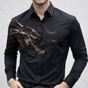 Może przedstawiać: Czarna koszula z długim rękawem ze złotym haftem smoka na lewym ramieniu i klatce piersiowej. Koszula ma klasyczny kołnierzyk i mankiety zapinane na guziki. Model ma na sobie czarny pasek i czarne spodnie.