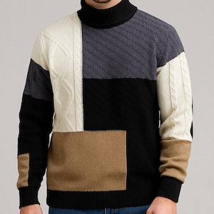 Könnte beinhalten: Ein Patchwork-Rollkragenpullover in verschiedenen Farben, darunter Schwarz, Weiß, Grau und Beige. Der Pullover hat ein geometrisches Design mit Zopfstrick- und Unifarbenen. Das Model trägt eine blaue Jeans.