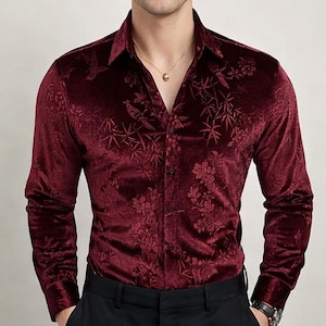 Puede incluir: Una camisa de terciopelo burdeos con un estampado floral. La camisa de manga larga tiene una botonadura y un cuello clásico. La camisa se combina con pantalones negros.