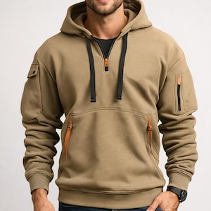 Puede incluir: Una sudadera con capucha de color beige con cremallera negra, cordones negros y dos bolsillos laterales. La sudadera tiene detalles de cuero naranja en los bolsillos y la cremallera. El modelo lleva un reloj negro y vaqueros azules.
