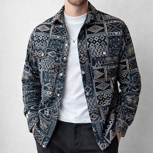 May include: A button-down shirt with a geometric pattern in shades of navy, teal, and tan. The shirt has a collared neckline and two chest pockets. The model is wearing a white t-shirt underneath and black pants.