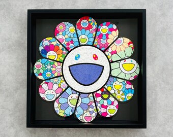 May include: A framed, colorful flower puzzle with a smiling face design. The puzzle features a variety of colors, including blue, pink, yellow, and green. The puzzle is set against a black background within a black frame.