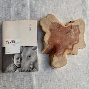 Puede incluir: Un libro con texto chino y una ilustración en escala de grises de una persona y un caballo. Junto a él, una rodaja de madera natural de forma única con un centro marrón rojizo y anillos exteriores de color marrón claro.