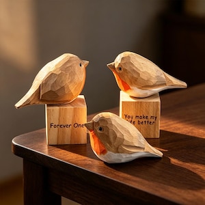 May include: Three carved wooden bird figurines with faceted surfaces, each featuring a reddish-orange chest and white belly. Two birds are perched on square wooden blocks, one inscribed with "Forever One" and the other with "You make my life better."