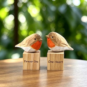May include: Two hand-carved wooden bird figurines with orange chests and white bellies, each perched on a square wooden block. The left block is engraved with the text Forever One, and the right block is engraved with the text One Heart.