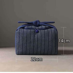 May include: A blue and white patterned fabric bag, approximately 22cm wide and 14cm tall, with a knotted handle and a button closure. The bag has a rectangular shape and is designed for carrying items.