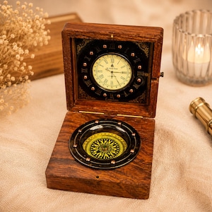 May include: A wooden box with a clock and compass. The clock has a cream-colored face with Roman numerals and black hands. The compass is below the clock, with a yellow and black design. The box is open, revealing the clock and compass.