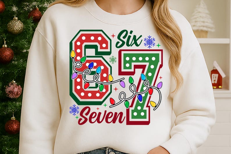 May include: Cream-colored sweatshirt with a festive design. The graphic features the number "67" in red and green, adorned with colorful string lights and the words "Six" and "Seven". Snowflakes add to the holiday theme.