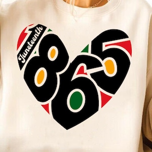 Puede incluir: Sudadera crema con un diseño en forma de corazón. El gráfico presenta los números "865" en negro, con acentos rojos, verdes y amarillos. La palabra "Juneteenth" está arqueada en la parte superior. Un diseño llamativo y colorido.