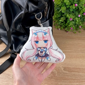 May include: A white plush keychain featuring an anime-style character with pink hair, blue eyes, and a maid outfit. The keychain is attached to a black backpack with a silver zipper.