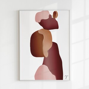 Op de afbeelding: Ingelijste abstracte kunstprint met gelaagde vormen in bruin, bordeaux en roze op een witte achtergrond. Het kunstwerk is rechtsonder gesigneerd. Minimalistisch en modern ontwerp, geschikt voor eigentijdse interieurs.