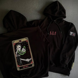 May include: Two black hoodies. One features a tarot card design with a skeleton and the text "THE DEVIL." The other has the text "4.5.0 project" in red and a small patch. Both have hoods and drawstrings.