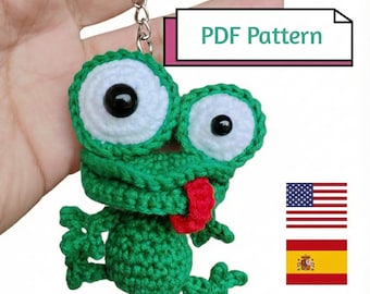 May include: A green crochet frog keychain with large white eyes, black pupils, and a red tongue sticking out. The item includes a metal keyring and a rectangular graphic with the text PDF Pattern, alongside icons of the United States and Spanish flags.