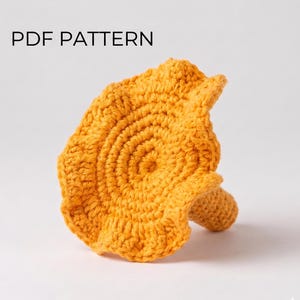 Könnte beinhalten: Ein goldgelber gehäkelter Pilz mit einem breiten, gerüschten Hut und einem strukturierten Stiel. Der Text PDF PATTERN ist in Schwarz in der oberen linken Ecke des Bildes aufgedruckt und weist auf ein digitales Handarbeitsdokument hin.