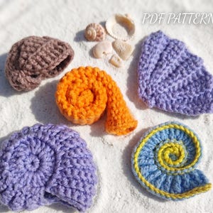 May include: A collection of five crocheted sea shell shapes in brown, orange, purple, and blue with yellow accents, accompanied by three small natural seashells and the text PDF PATTERN. The crochet items feature textured yarn stitches.