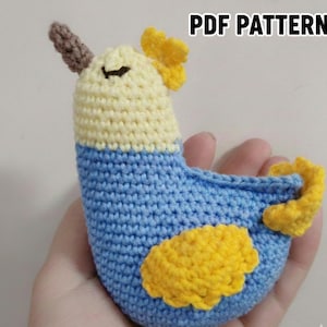 Op de afbeelding: Een handgemaakte gehaakte vogel in blauw, geel en crème. De vogel heeft een gele vleugel en staart, een crèmekleurige kop en een blauw lichaam. De tekst "PDF PATTERN" staat in de rechterbovenhoek.
