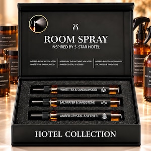 May include: A black gift box containing three amber glass spray bottles labeled White Tea & Sandalwood, Saltwater & Sandstone, and Amber Crystal & Vetiver. The box lid features the text Room Spray Inspired by 5-Star Hotel and Hotel Collection.