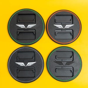 May include: Four black, circular objects featuring a white wing logo and two rectangular cutouts. Each has a coloured border: green, orange, and two with green. The background is yellow.