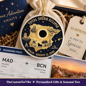 May include: A round ceramic ornament featuring a gold map of Spain with a black solar eclipse, text reading TOTAL SOLAR ECLIPSE SPAIN AUGUST 12, 2026, a boarding pass from Madrid to Barcelona, a gift tag saying SURPRISE! A TRIP TO SPAIN 2026, and a card.