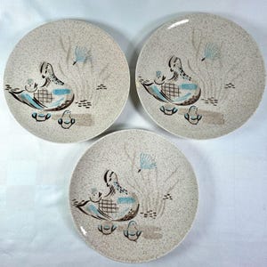 Puede incluir: Tres platos redondos de cerámica con un acabado beige moteado. Cada plato presenta una ilustración gráfica central de una madre pájaro con dos polluelos, acentuada con detalles en azul y marrón, junto a motivos vegetales estilizados y pequeñas marcas marrones.