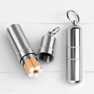 Puede incluir: Tres pitilleras de acero inoxidable. Una está abierta, mostrando cigarrillos. Las otras dos están cerradas, una con un llavero. Las pitilleras son cilíndricas y tienen un acabado pulido. Las pitilleras son de metal.