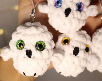 May include: Handmade white crochet owl ornaments with colorful eyes and black beaks. Each owl has a unique eye color, including green, blue, and yellow. These small, fluffy owls are attached to a white string.
