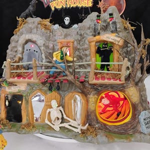 May include: A Haunted Fun House miniature display featuring a rocky mountain structure with a wolf, a skeleton, and a sign reading Haunted Fun House. The scene includes a bridge, a figure in a yellow shirt, a black-clad figure, and a red-clad figure.