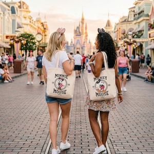 Może przedstawiać: Dwie kobiety idą ulicą z cegieł, każda z beżową torbą. Jedna torba przedstawia Minnie Mouse, druga Myszka Miki, obie w stylu vintage. Torby mają czarne uchwyty i są zadrukowane imieniem i wizerunkiem postaci.