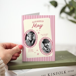 以下が含まれることがあります： 「ALSO BORN IN May」のテキストが入った、ピンクと白のストライプのグリーティングカード。カードには、楕円形のフレームに入った歴史上の人物の2つの白黒ポートレートが描かれています。カードは緑色の本の上に置かれています。