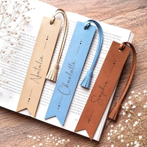 Könnte beinhalten: Drei rechteckige Lesezeichen in Beige, Hellblau und Braun, jeweils mit passender Lederquaste, spitzem unterem Rand und einem vertikalen Liniendesign mit Punkten. Die Namen Natalie, Charlotte und Sophia sind in schwarzer Schrift aufgedruckt.