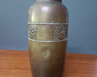 May include: A vintage brass vase with a cylindrical body and a slightly flared base. The vase features a decorative band with a repeating leaf design. The top rim has a series of small, raised dots. The vase has a tarnished, aged appearance.