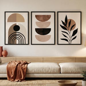 Puede incluir: Tres impresiones artísticas abstractas enmarcadas. Las impresiones presentan formas geométricas en tonos neutros de marrón, beige y negro. Una impresión tiene un diseño de planta. Los marcos son negros y el arte se exhibe sobre un sofá beige.