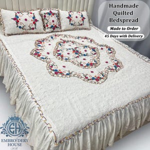 Op de afbeelding: Handgemaakte witte gewatteerde sprei met bloemenborduurwerk en bijpassende kussens. De sprei heeft een geplooid rokje en decoratieve afwerking. De afbeelding bevat de tekst "Handmade Quilted Bedspread Made to Order 45 Days with Delivery."