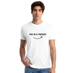 May include: White t-shirt with the text "VIVE EN EL PRESENTE" in black, above a curved line with an arrow pointing right. The shirt is a crew neck style.