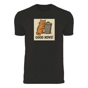 May include: Black t-shirt featuring a cartoon illustration. The illustration shows an orange tabby cat hugging a smiling trash can. The words "GOOD NEWS!" are printed below the image.