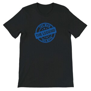 May include: Black t-shirt with a blue circular graphic. The graphic reads "THE MAN THE LEGEND THE MYTH" in a stamp-like design. The shirt is made of a soft material and has short sleeves.