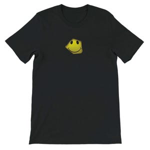 May include: Black t-shirt featuring a yellow smiley face graphic. The smiley face has a distressed, textured appearance. The t-shirt has short sleeves and a crew neck. This casual tee is suitable for everyday wear.