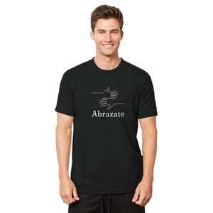 May include: Black t-shirt with a white graphic of two hands embracing, and the word "Abrazate" below the graphic. The shirt is made of a soft material.
