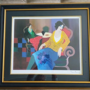 May include: Framed art print featuring two figures in a cafe setting. One figure is seated in a red chair, wearing a yellow top and blue skirt. The other figure is seated at a table, wearing a green top and red skirt. The artwork is signed in the bottom right corner.