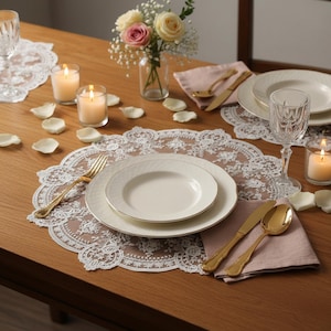 Op de afbeelding: Een gedekte tafel met witte borden, gouden bestek en een roze servet. De tafel is versierd met kaarsen, rozenblaadjes en een vaas met bloemen. De placemat is van wit kant.