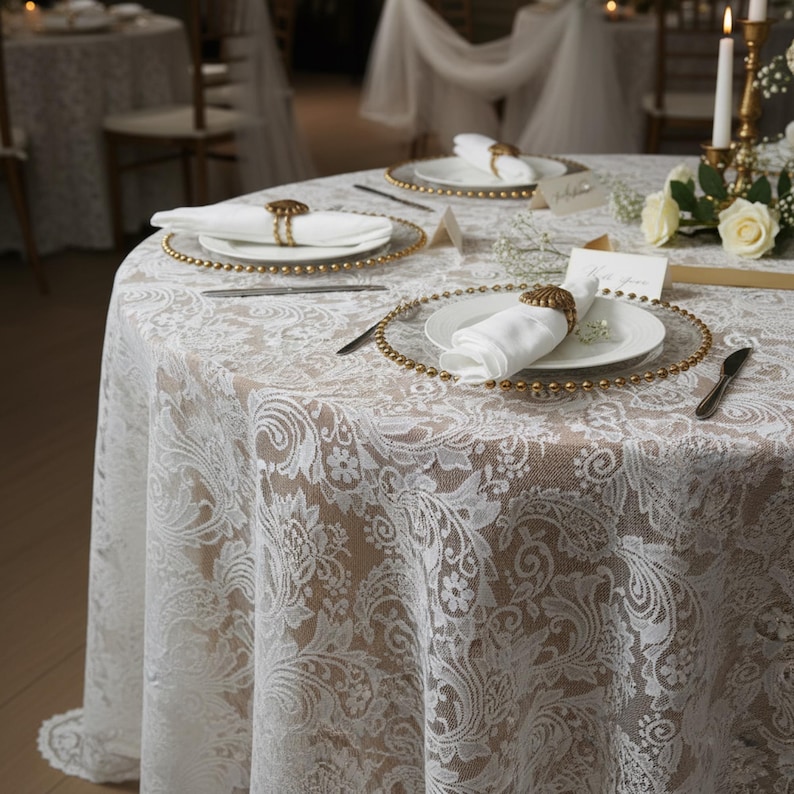 Puede incluir: Una mesa redonda preparada para un evento formal, cubierta con un mantel de encaje blanco. Cada cubierto incluye un plato blanco, una servilleta blanca doblada y un cargador con cuentas doradas. Los servilleteros dorados y la cuberter&iacute;a completan el elegante look.