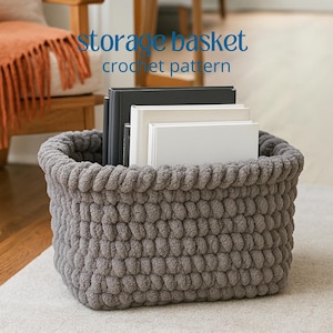 Puede incluir: Una cesta de almacenamiento rectangular de ganchillo gris llena de libros. La cesta tiene un aspecto grueso y texturizado y un borde superior enrollado. El texto "storage basket crochet pattern" es visible en la imagen.