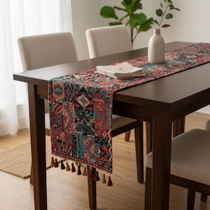 May include: A dark brown wooden dining table with a colorful patterned table runner. The runner features a patchwork design in red, blue, and beige with decorative tassels. A white vase with greenery and folded napkins are on the table.